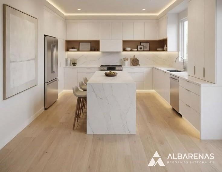 Cocina después de la reforma de Albarenas: muebles blancos, isla con mesada de mármol y piso de madera